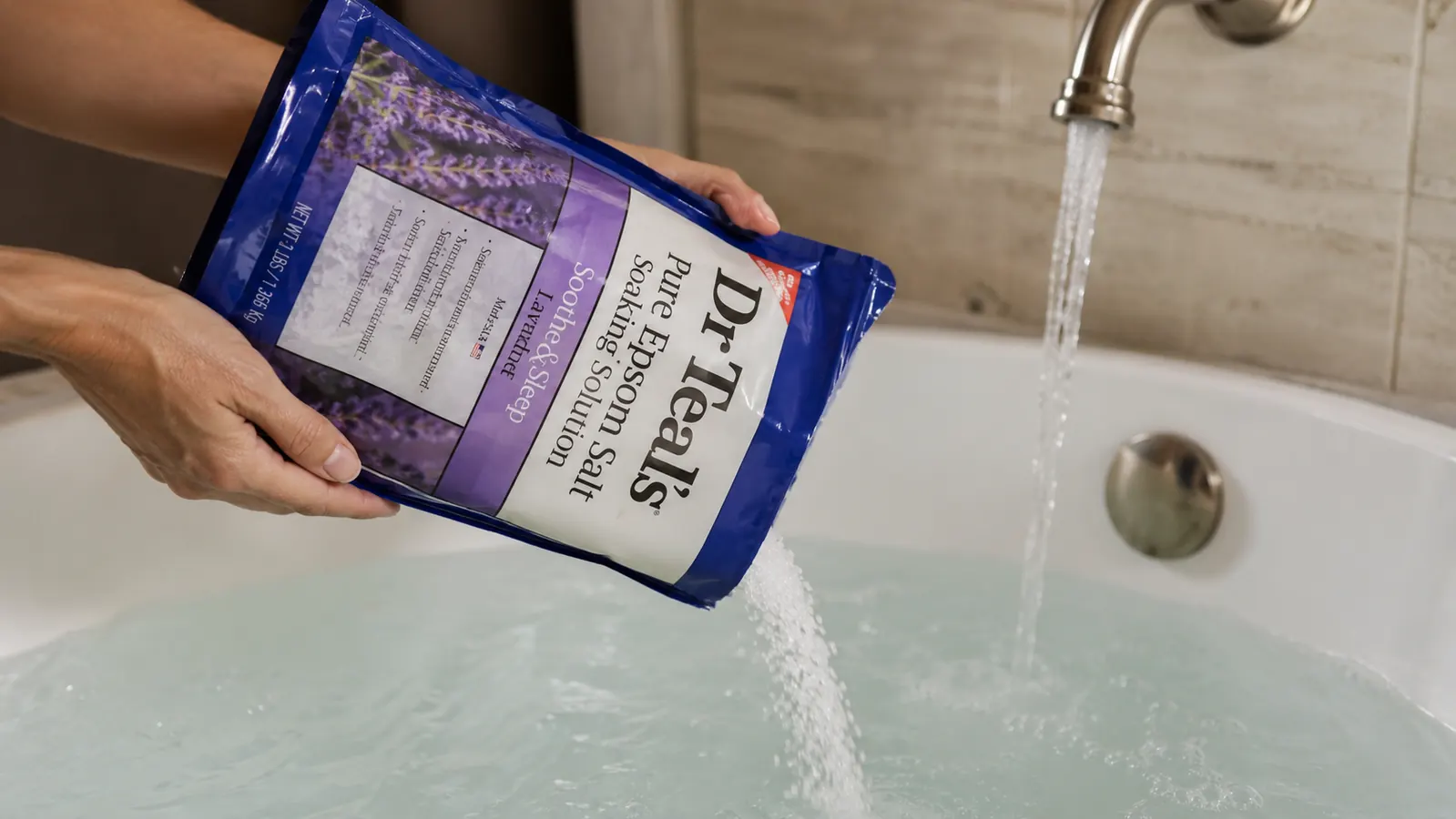 Hand pouring epsom salt from a carton into a steaming bathtub
